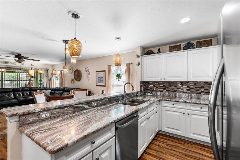 A kitchen with white cabinets, granite countertops, and a breakfast bar overlooking a living area — 4436 TURNBERRY LANE, LAKE WALES, FL