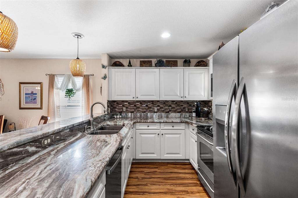 A kitchen features white cabinets, granite countertops, a stainless steel refrigerator, and wood-look flooring — 4436 TURNBERRY LANE, LAKE WALES, FL