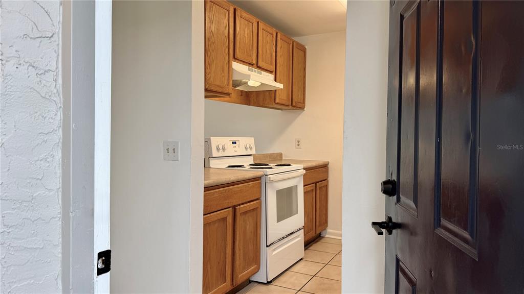 A kitchen with wood cabinets, a white stove, and tile flooring viewed through a doorway — 101 CORY LANE, WINTER SPRINGS, FL