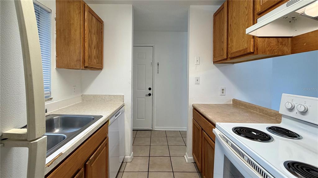 A galley kitchen features oak cabinets, white appliances, laminate countertops, and tile flooring — 101 CORY LANE, WINTER SPRINGS, FL