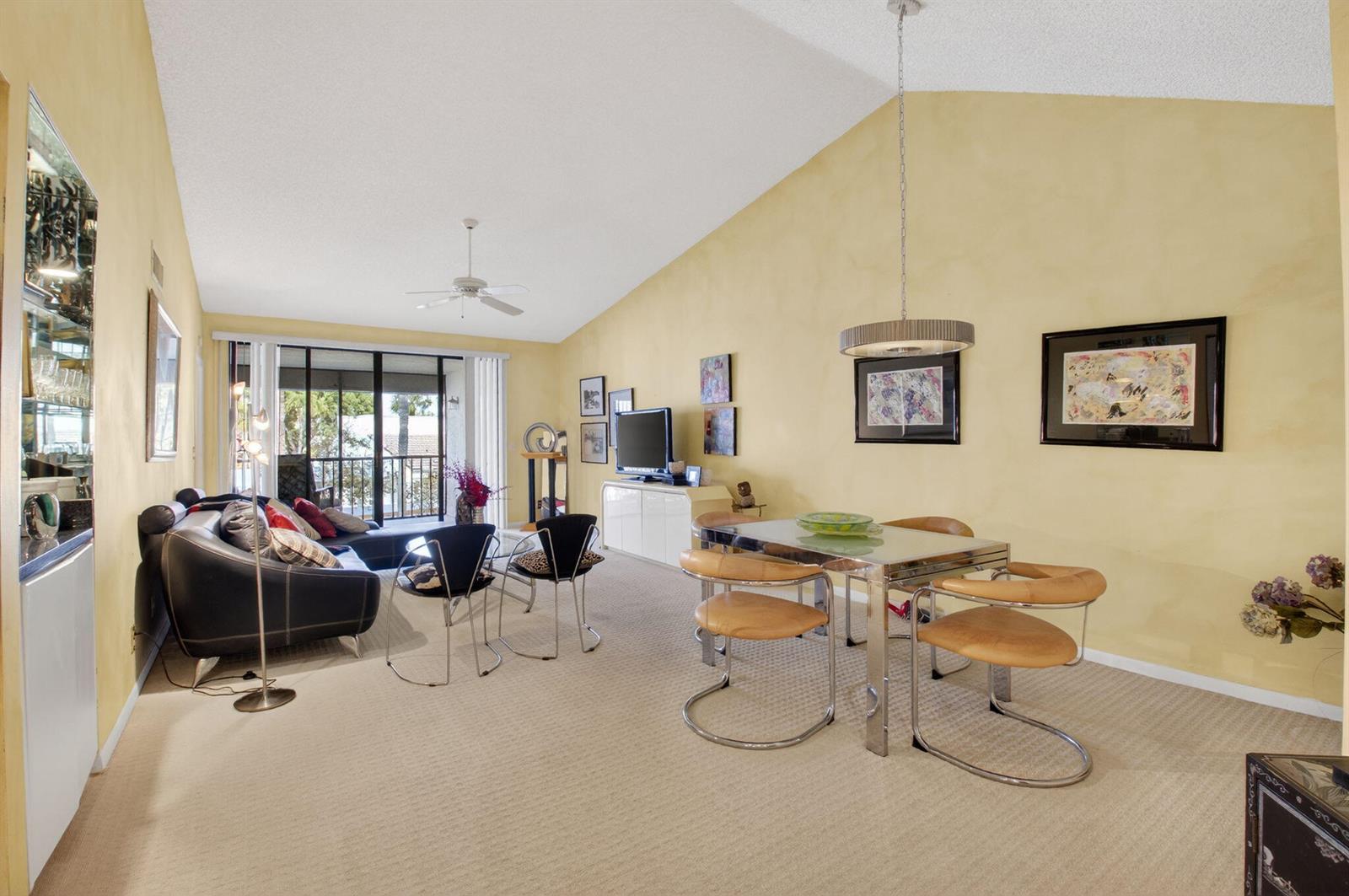A living and dining area with vaulted ceilings, yellow walls, carpeted floors, and a balcony — 7509 Glendevon Lane # 1006, Delray Beach FL 33446, DELRAY BEACH, FL