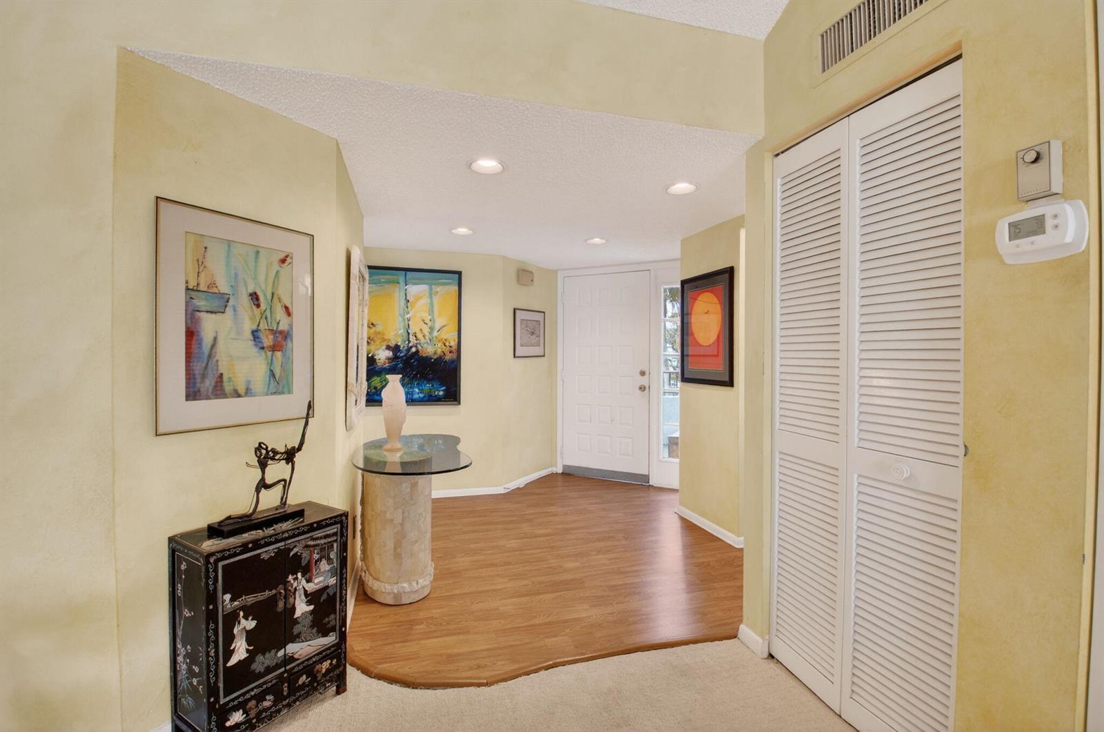An entryway features yellow walls, wood-look flooring, a glass-topped pedestal table, and louvered closet doors — 7509 Glendevon Lane # 1006, Delray Beach FL 33446, DELRAY BEACH, FL