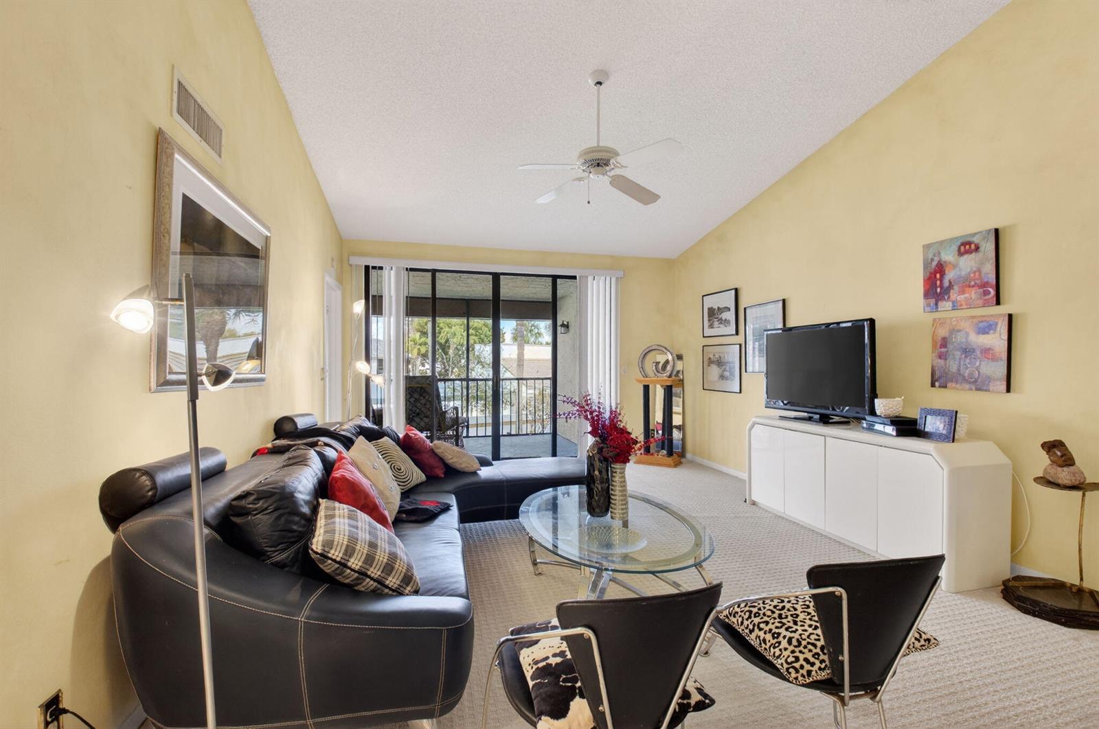 A living room features a black sectional sofa, glass coffee table, and a television console — 7509 Glendevon Lane # 1006, Delray Beach FL 33446, DELRAY BEACH, FL