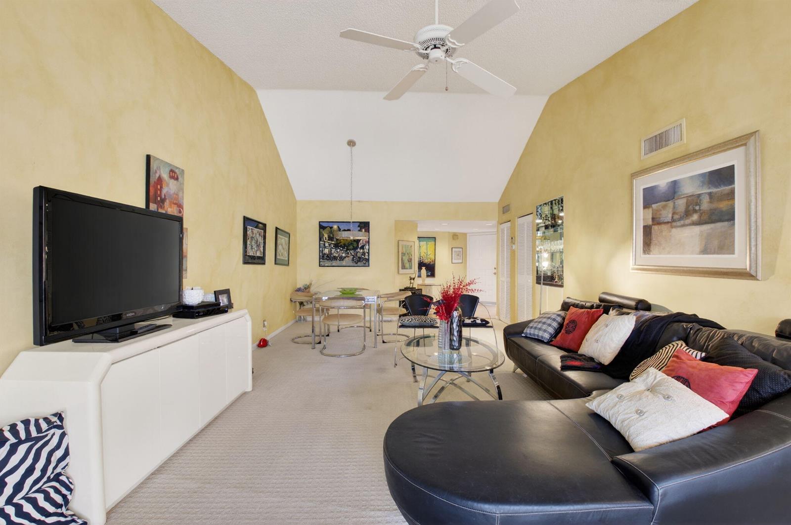 A living room with yellow walls, a vaulted ceiling, a black sectional, and dining area — 7509 Glendevon Lane # 1006, Delray Beach FL 33446, DELRAY BEACH, FL
