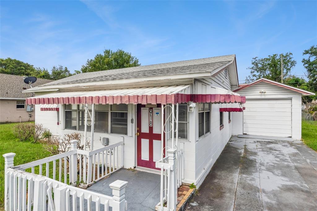 A white house with a red door, metal awning, and attached garage under a blue sky — 918 S GOLDWYN AVENUE, ORLANDO, FL
