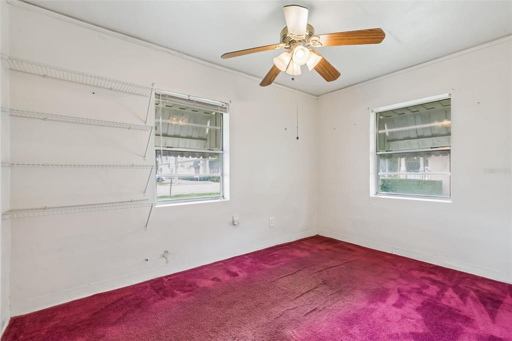 An empty bedroom features white walls, a ceiling fan, wire shelving, and magenta carpeting — 918 S GOLDWYN AVENUE, ORLANDO, FL