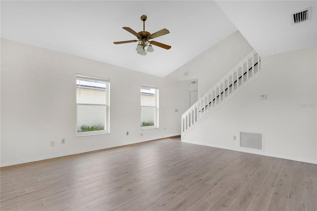A living room features light wood-look flooring, white walls, a ceiling fan, and a staircase — 11842 ATLIN DRIVE, ORLANDO, FL