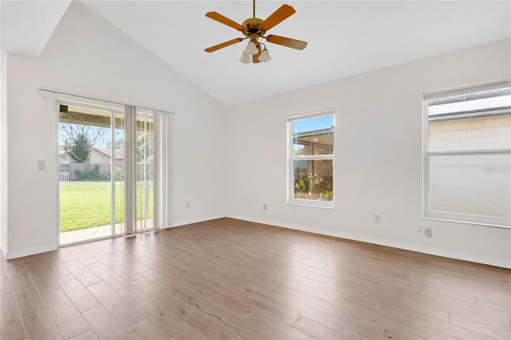 An empty room with light wood-look tile flooring, a vaulted ceiling, and sliding glass doors — 11842 ATLIN DRIVE, ORLANDO, FL