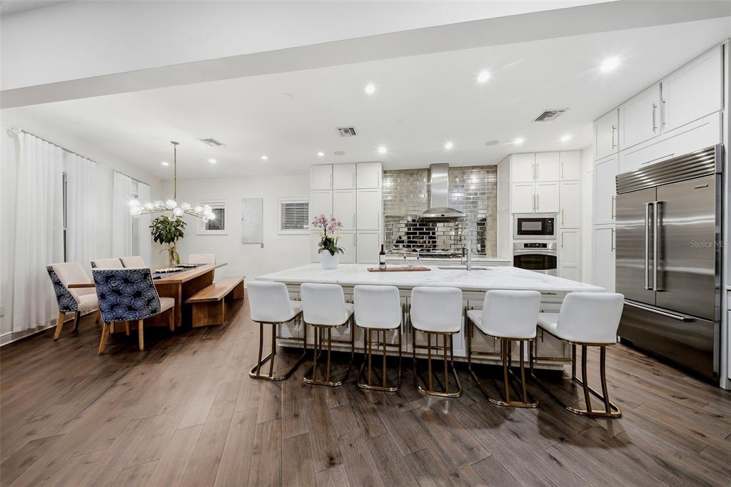 A modern kitchen features a large marble island with white barstools and dark wood flooring — 2711 W TRILBY AVENUE, TAMPA, FL