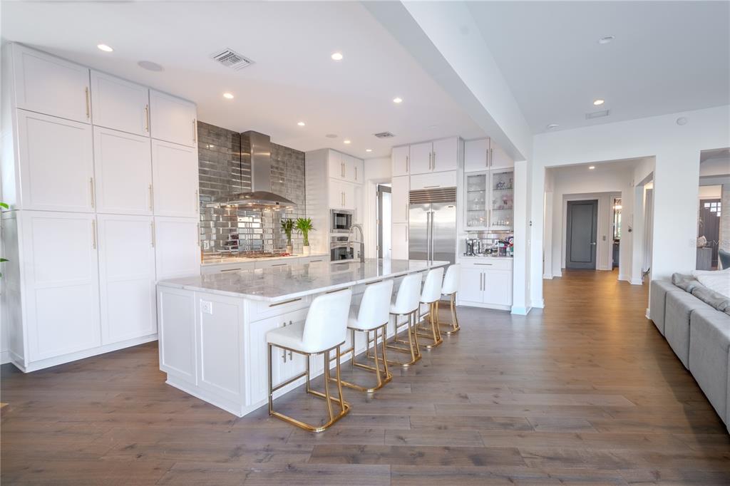 A modern kitchen features white cabinetry, a marble-topped island with bar stools, and wood flooring — 2711 W TRILBY AVENUE, TAMPA, FL