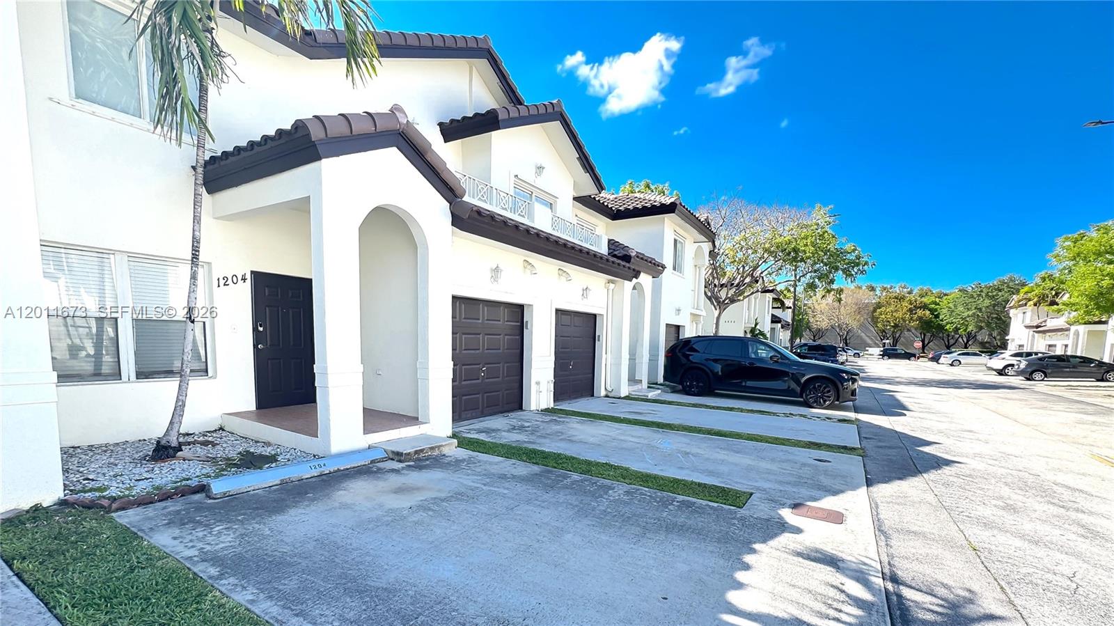 A two-story townhouse exterior features a white facade, dark brown garage doors, and a driveway — 8902 NW 109th Ct # 1204, Doral FL 33178, DORAL, FL