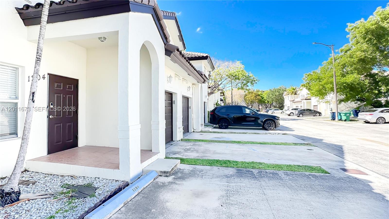 The exterior of a white townhouse features a dark brown door and a concrete driveway — 8902 NW 109th Ct # 1204, Doral FL 33178, DORAL, FL