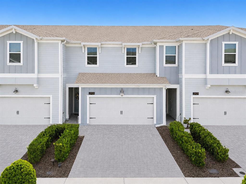 A light blue two-story townhouse exterior with three white garage doors and paved driveways — 2931 SENTENCE STREET, KISSIMMEE, FL