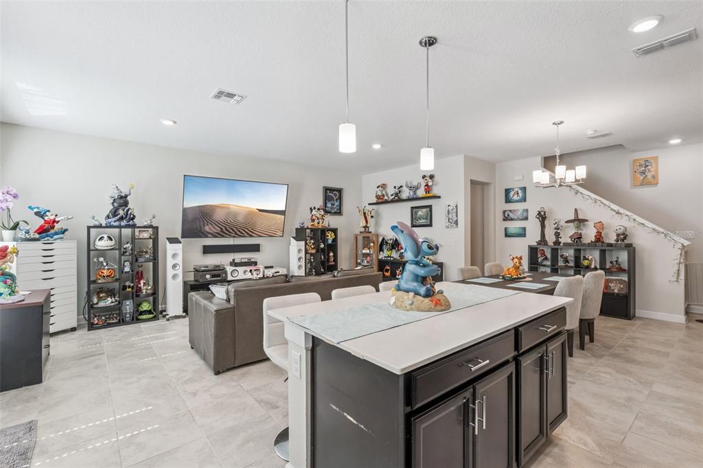 An open-concept living room and kitchen featuring tile flooring, dark cabinetry, and numerous collectible figures — 2931 SENTENCE STREET, KISSIMMEE, FL