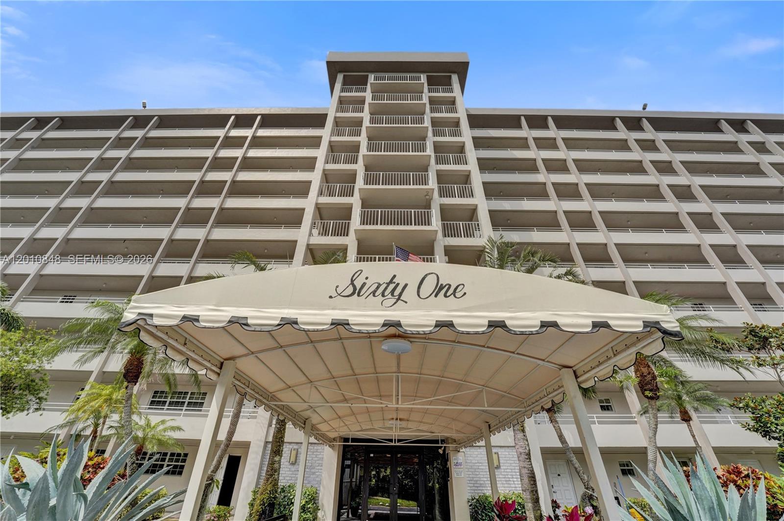 The exterior of a multi-story apartment building features a beige awning labeled Sixty One — 575 Oaks Ln # 508, Pompano Beach FL 33069, POMPANO BEACH, FL