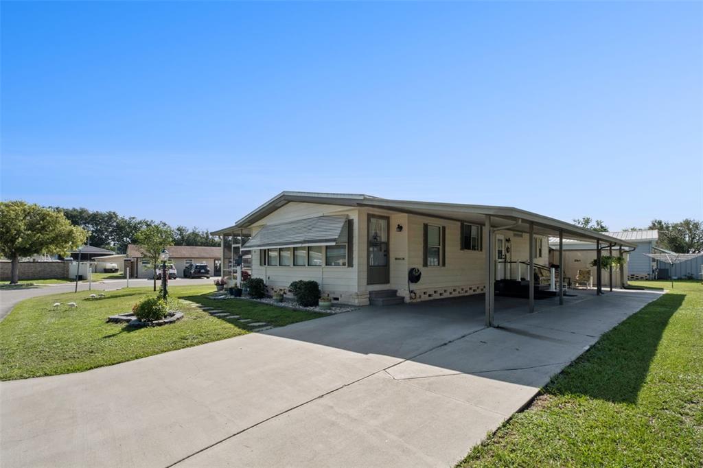 A single-story manufactured home with a concrete driveway and an attached carport under a blue sky — 301 LAKEVIEW DRIVE, OSTEEN, FL