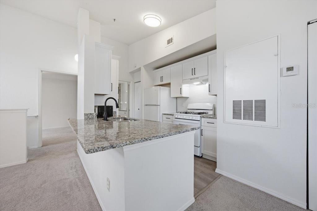 A kitchen features white cabinets, granite countertops, a breakfast bar, and white appliances — 1612 COLUMBIA ARMS CIRCLE UNIT 237, KISSIMMEE, FL