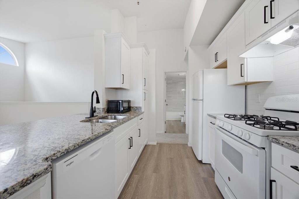 A kitchen features white cabinets, granite countertops, white appliances, and wood-look flooring — 1612 COLUMBIA ARMS CIRCLE UNIT 237, KISSIMMEE, FL