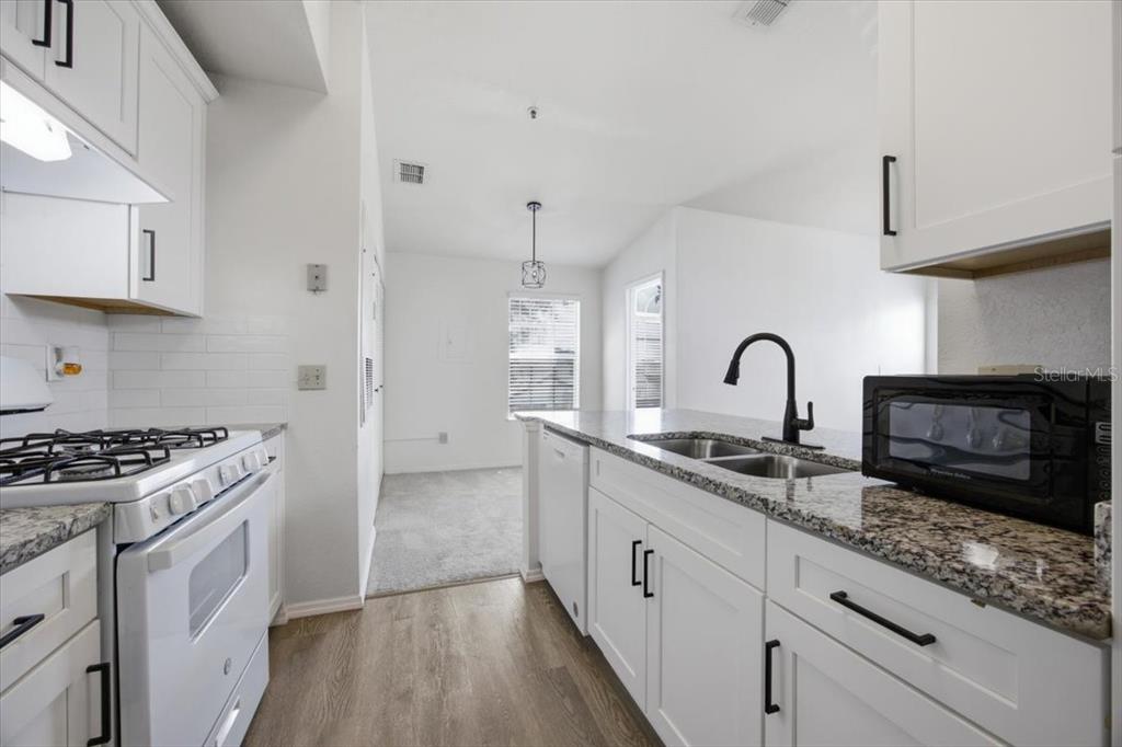A kitchen with white cabinets, granite countertops, and a gas stove, opening to a carpeted area — 1612 COLUMBIA ARMS CIRCLE UNIT 237, KISSIMMEE, FL