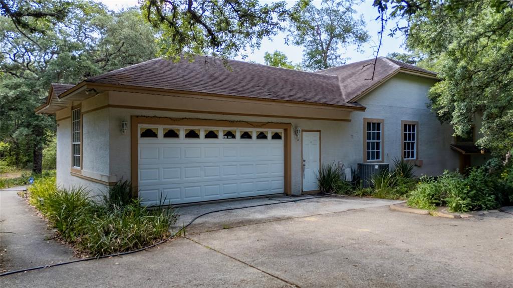 A detached garage with a white door, a side entry, and stucco walls under trees — 6781 W LIVINGSTON STREET, ORLANDO, FL