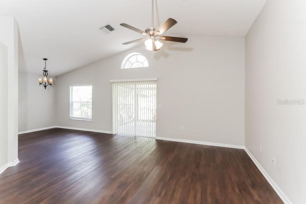 An empty living room features dark wood-look flooring, a vaulted ceiling, and a ceiling fan — 1846 TWISTING LANE, WESLEY CHAPEL, FL