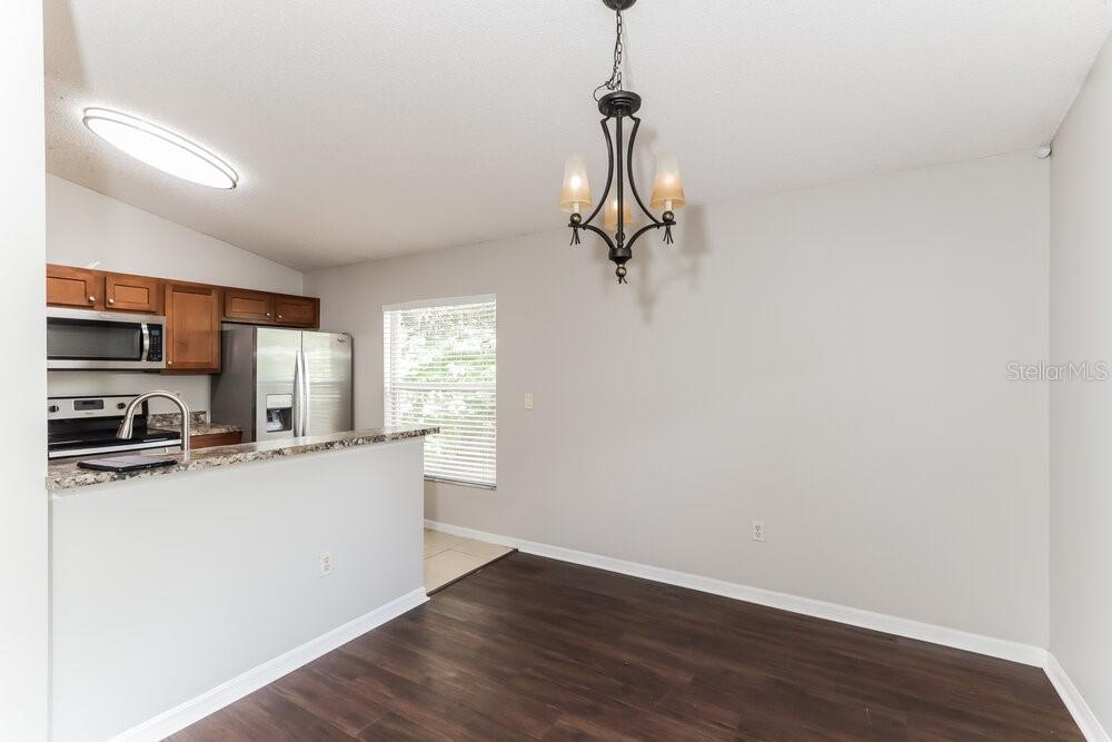 A dining area with a chandelier, dark wood flooring, and an adjacent kitchen with cabinets — 1846 TWISTING LANE, WESLEY CHAPEL, FL
