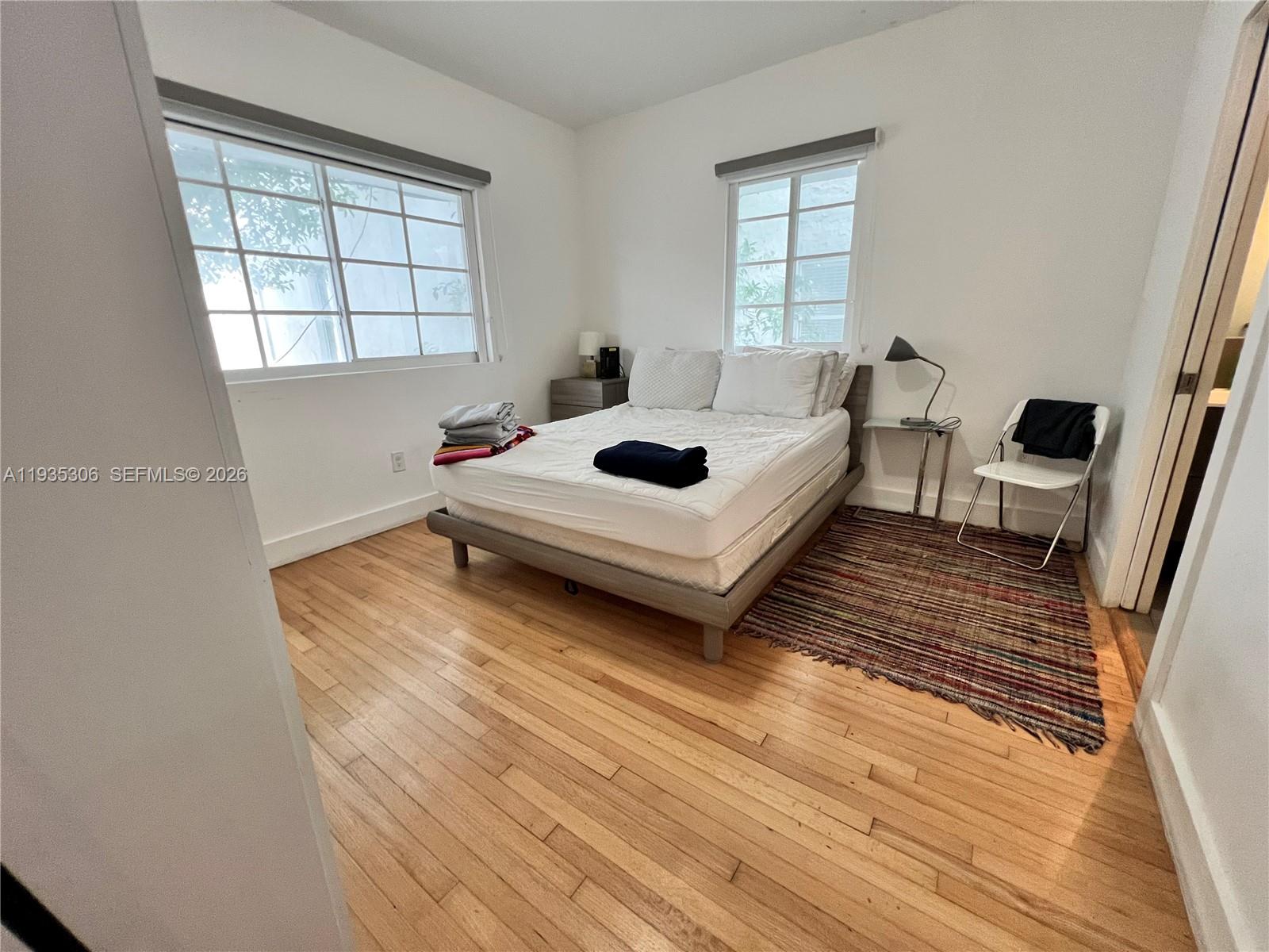 A bedroom features a bed, hardwood floors, two windows, and a small chair — 600 15th St # 10, Miami Beach FL 33139, MIAMI BEACH, FL