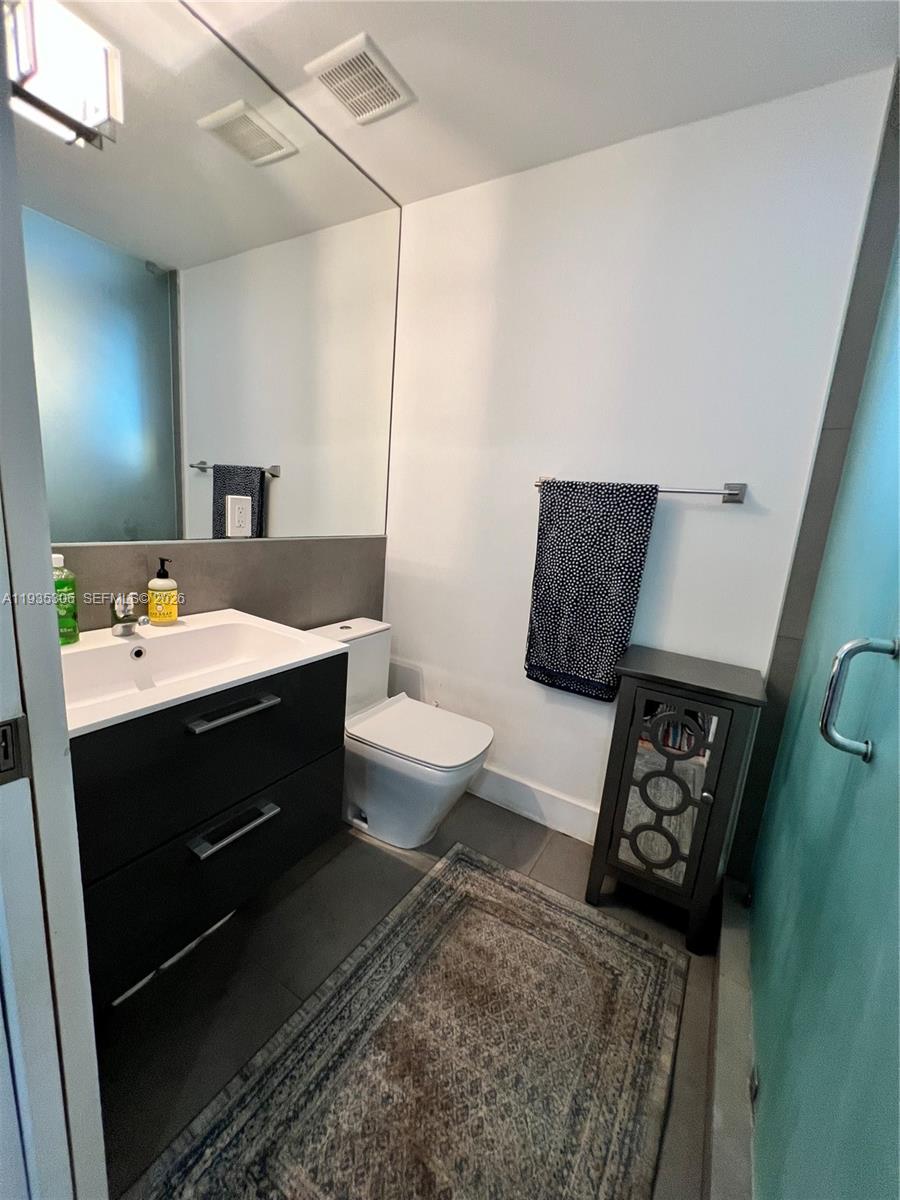 A modern bathroom features a dark vanity, a white toilet, and a patterned area rug — 600 15th St # 10, Miami Beach FL 33139, MIAMI BEACH, FL