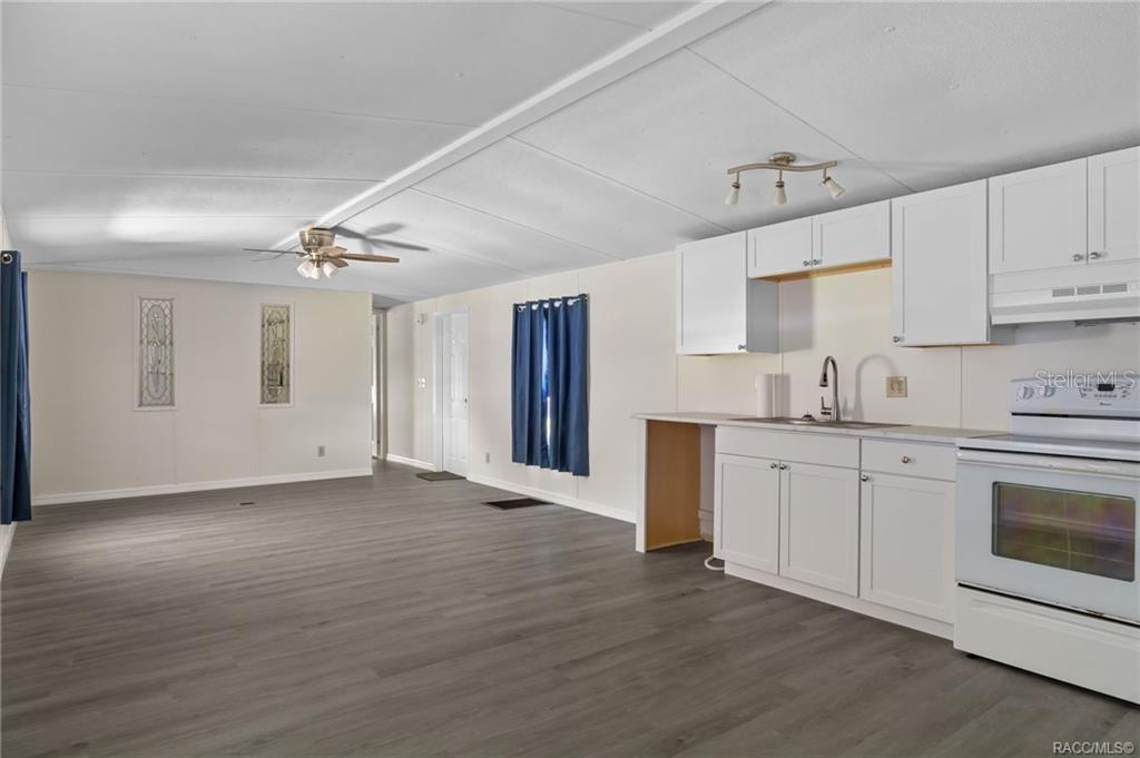 An open-concept kitchen and living area featuring white cabinets, light flooring, and a ceiling fan — 9771 SE 171ST PLACE, SUMMERFIELD, FL