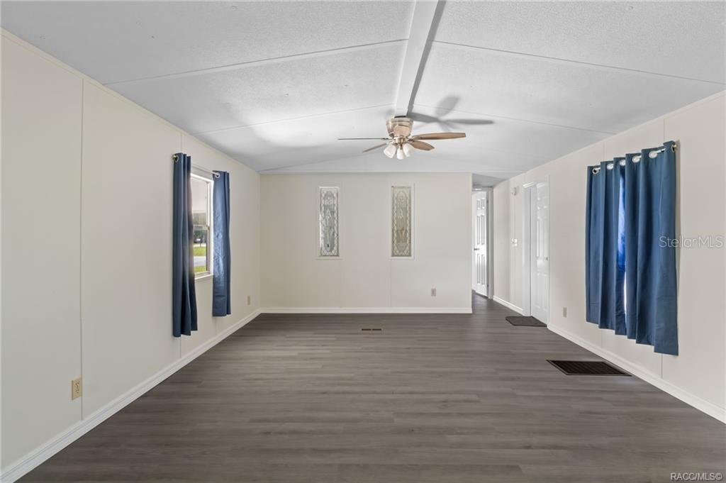An empty room features light walls, dark wood-look flooring, blue curtains, and a ceiling fan — 9771 SE 171ST PLACE, SUMMERFIELD, FL