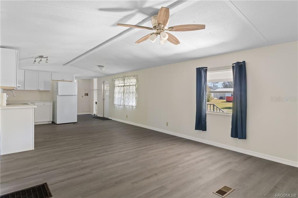 An open-concept living area features wood-look flooring, white walls, a ceiling fan, and a kitchen — 9771 SE 171ST PLACE, SUMMERFIELD, FL