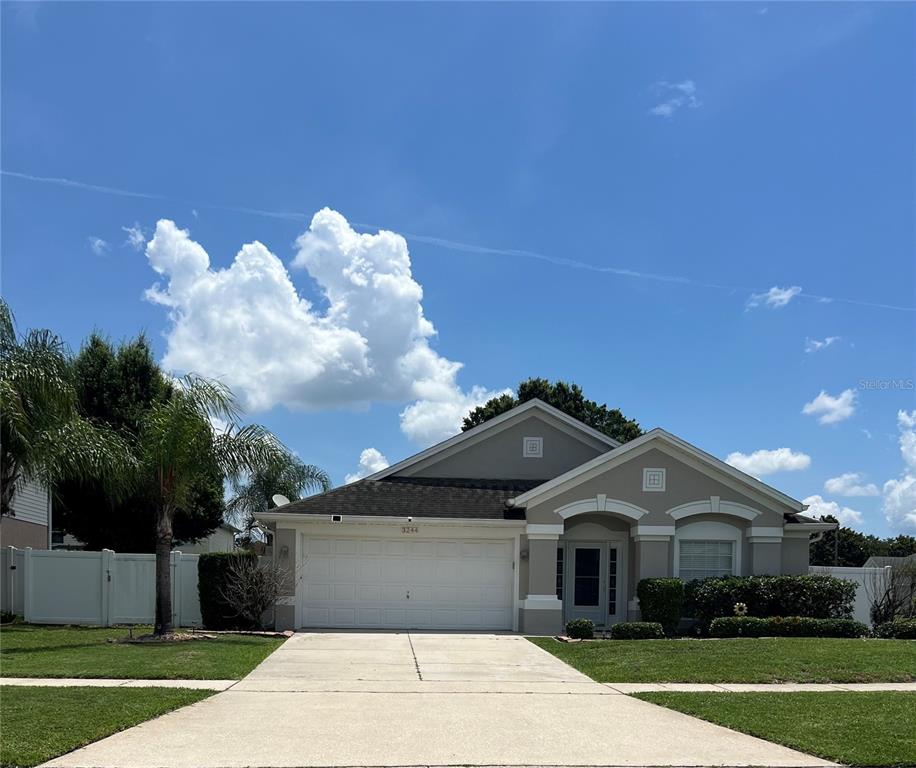 A single-story suburban house with a two-car garage, beige stucco siding, and a concrete driveway — 3244 HERONS POINT CIRCLE, KISSIMMEE, FL