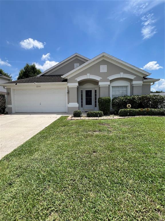 A beige single-story house with a two-car garage and a front lawn under a sky — 3244 HERONS POINT CIRCLE, KISSIMMEE, FL