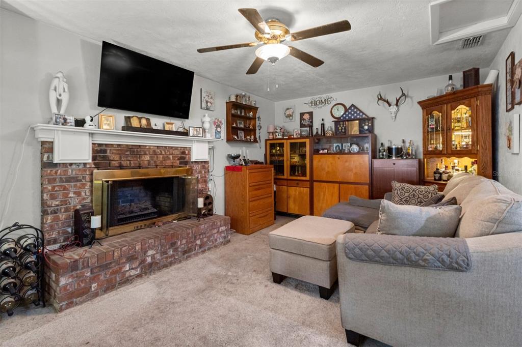 A living room features a brick fireplace, a television, a ceiling fan, and wooden cabinetry — 1529 NW 143RD STREET, GAINESVILLE, FL