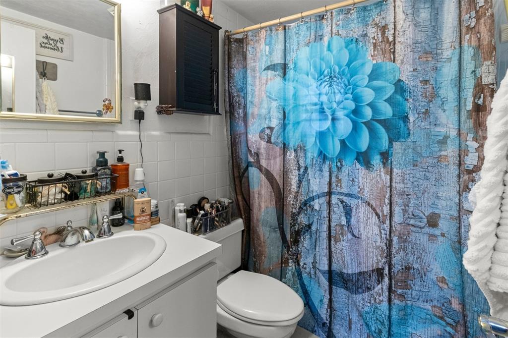 A bathroom features a white vanity, a toilet, and a shower curtain with a blue flower — 1529 NW 143RD STREET, GAINESVILLE, FL