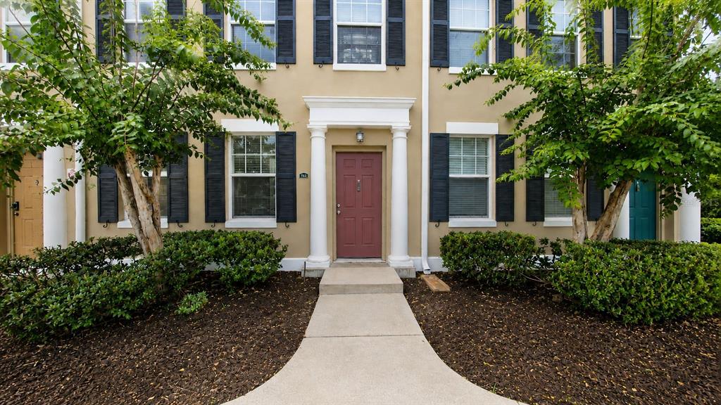 A red front door is centered between two white columns on a tan townhouse exterior — 763 SIENA PALM DRIVE, CELEBRATION, FL