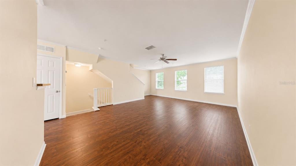 An empty living room features wood-look flooring, beige walls, a ceiling fan, and three windows — 763 SIENA PALM DRIVE, CELEBRATION, FL