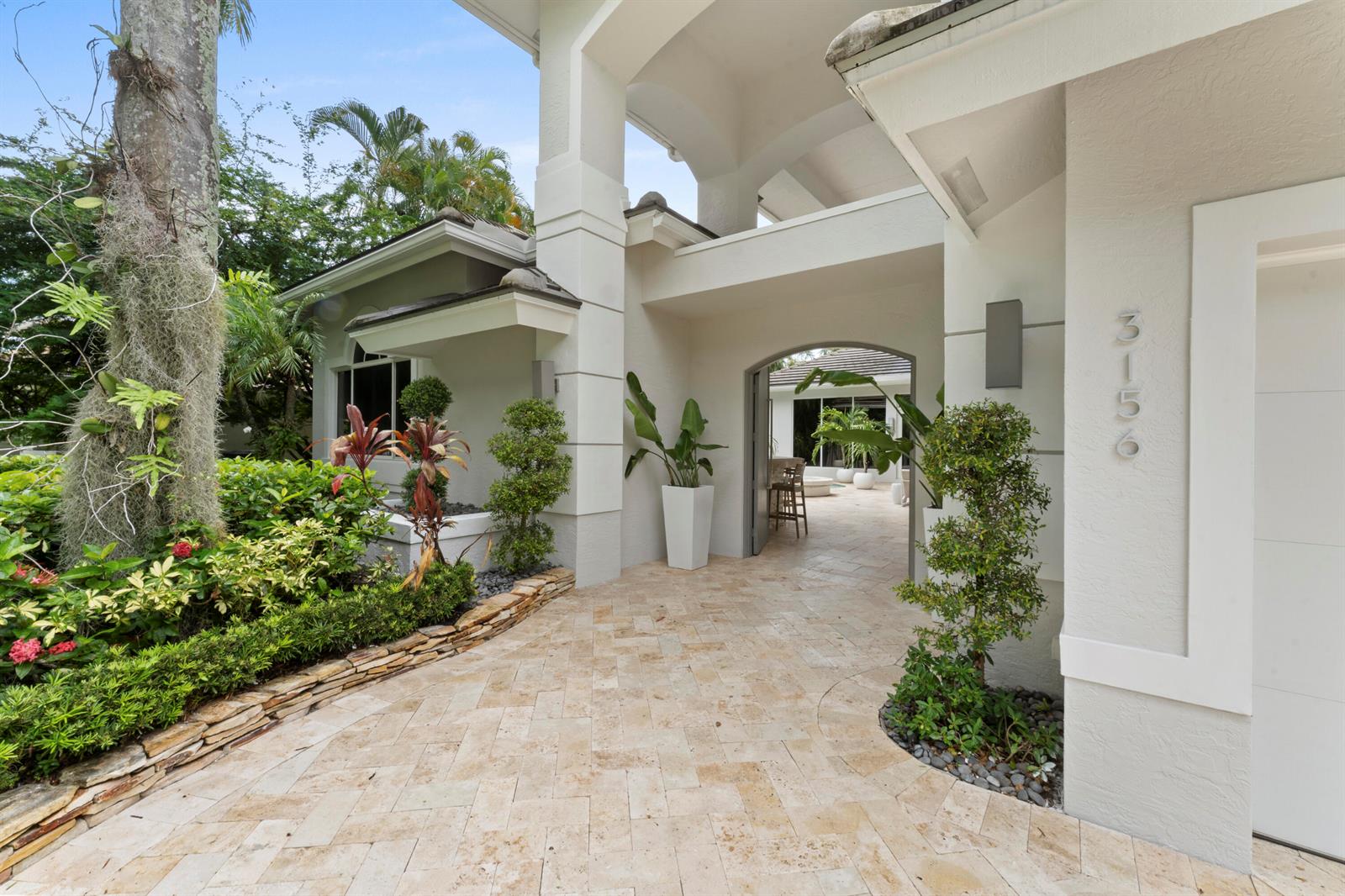 A paved walkway leads to an arched entryway of a white house with tropical landscaping — 3156 NW 61st Street, Boca Raton FL 33496, BOCA RATON, FL