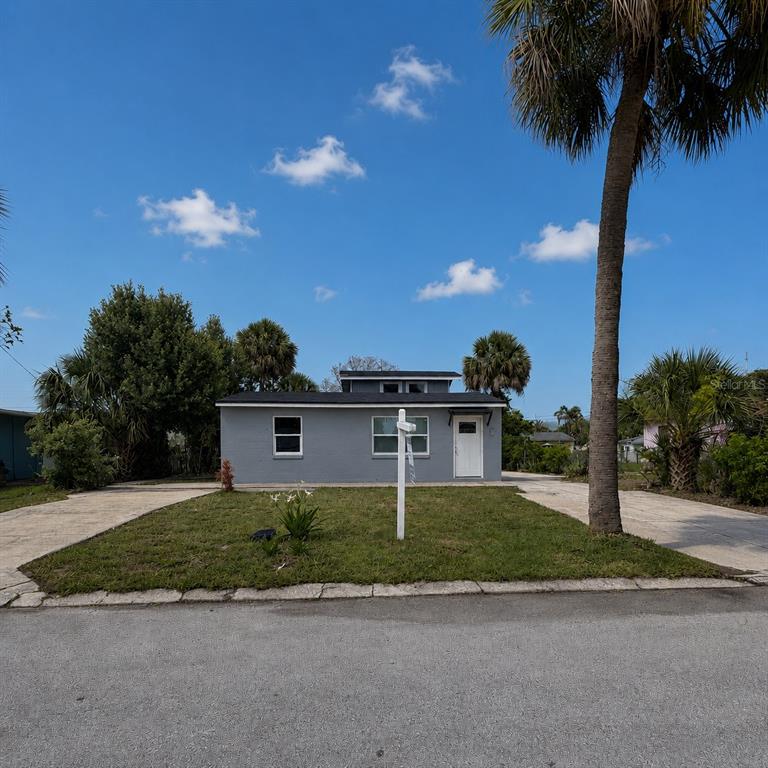A single-story gray house with a white door and two driveways sits under a blue sky — 1125 GAINEY DRIVE, MELBOURNE, FL