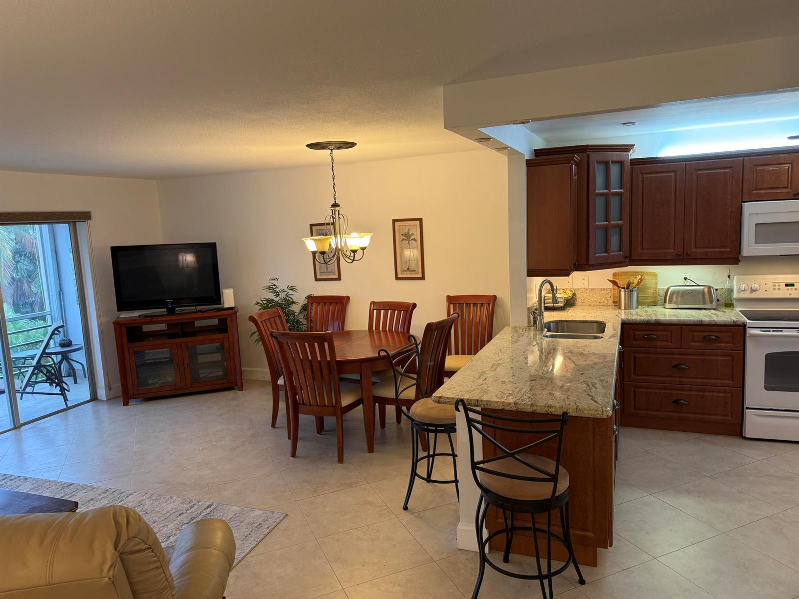 An open-concept kitchen and dining area features wood cabinetry, granite countertops, and tile flooring — 300 NE 14th Avenue # 411, Hallandale Beach FL 33009, HALLANDALE BEACH, FL