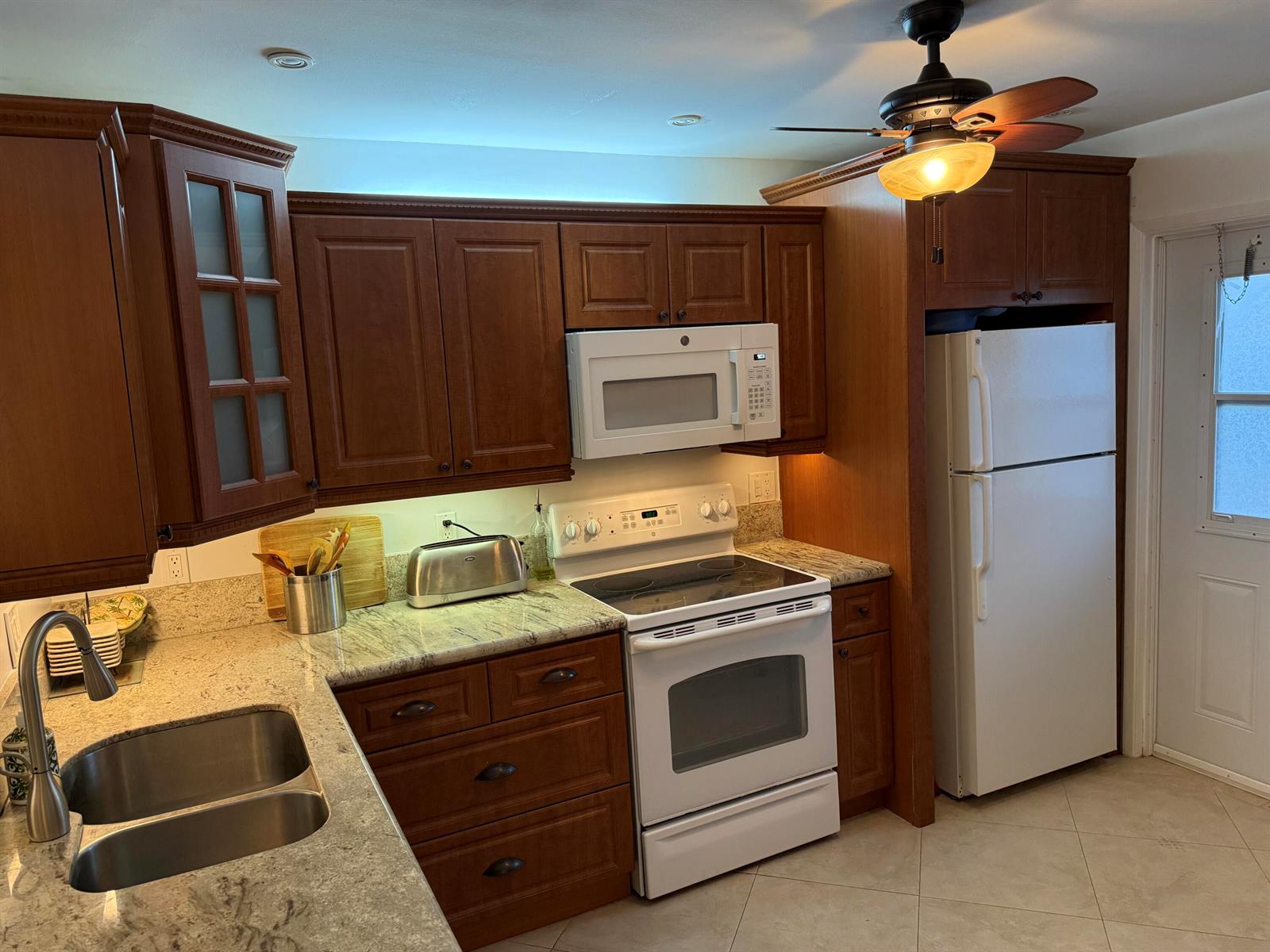 A kitchen features dark wood cabinets, granite countertops, white appliances, and a ceiling fan — 300 NE 14th Avenue # 411, Hallandale Beach FL 33009, HALLANDALE BEACH, FL