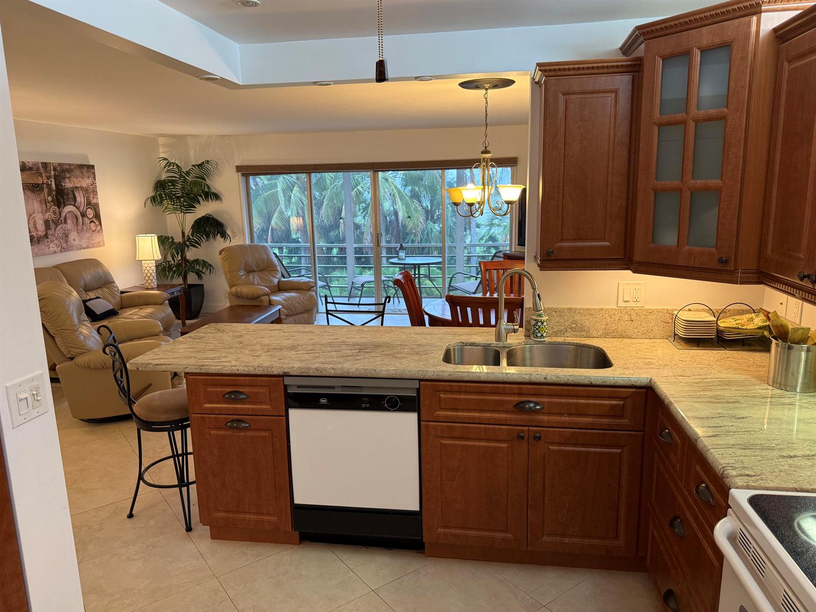 A kitchen with wood cabinets and granite countertops overlooks a living area and outdoor balcony — 300 NE 14th Avenue # 411, Hallandale Beach FL 33009, HALLANDALE BEACH, FL