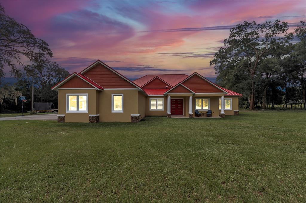 A single-story house with a red metal roof and tan stucco exterior sits on grass — 14742 SW 4TH AVENUE, OCALA, FL