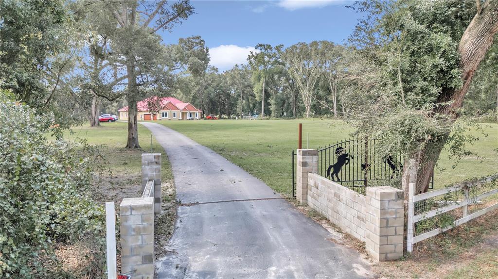 A long paved driveway leads to a house with a red roof through a gated entrance — 14742 SW 4TH AVENUE, OCALA, FL