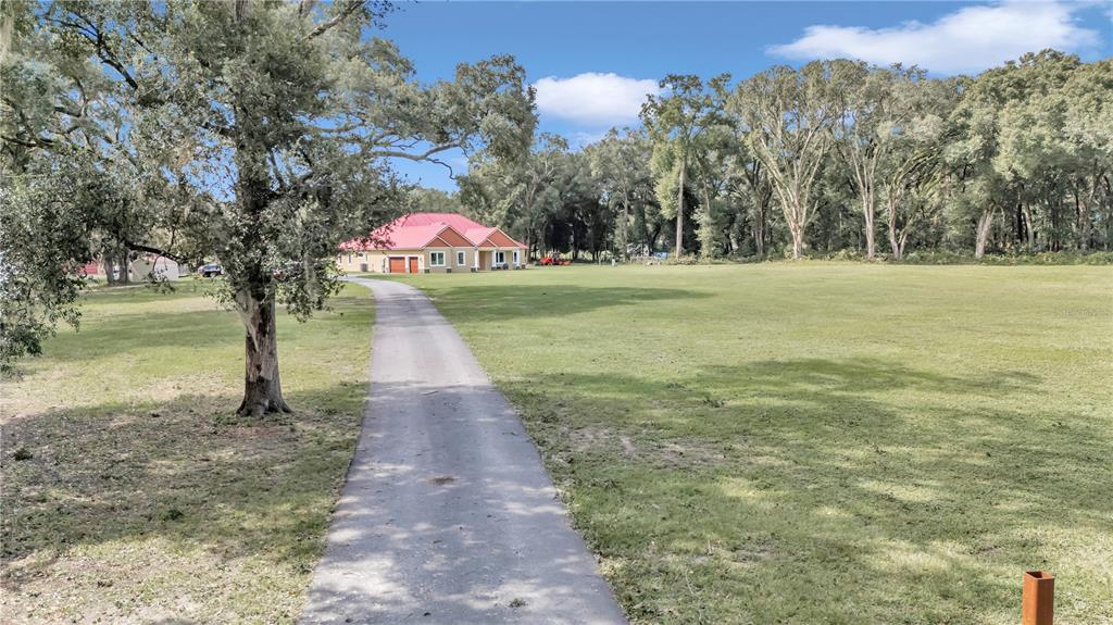 A long paved driveway leads to a house with a red roof on a grassy lot — 14742 SW 4TH AVENUE, OCALA, FL