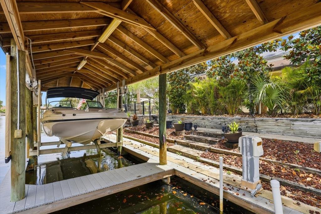 A boat sits on a lift under a wooden roof next to a terraced garden — 25 COTTONWOOD COURT, PALM COAST, FL