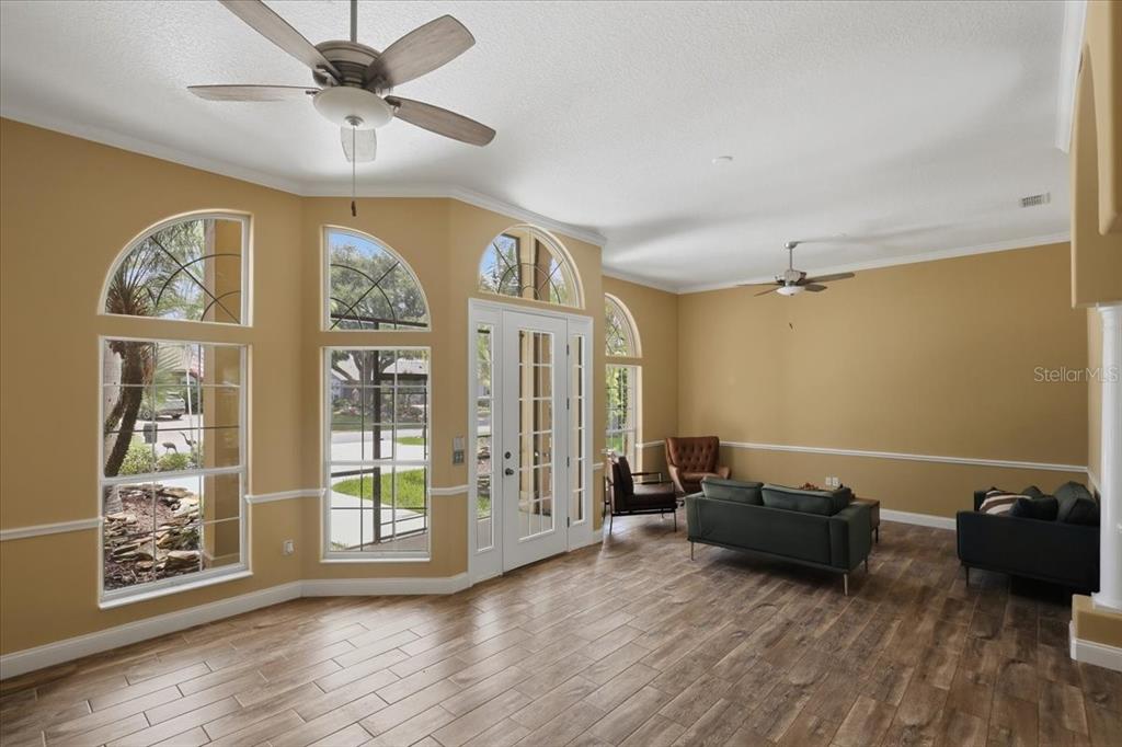 A living room with wood-look tile floors, yellow walls, and large arched windows — 25 COTTONWOOD COURT, PALM COAST, FL