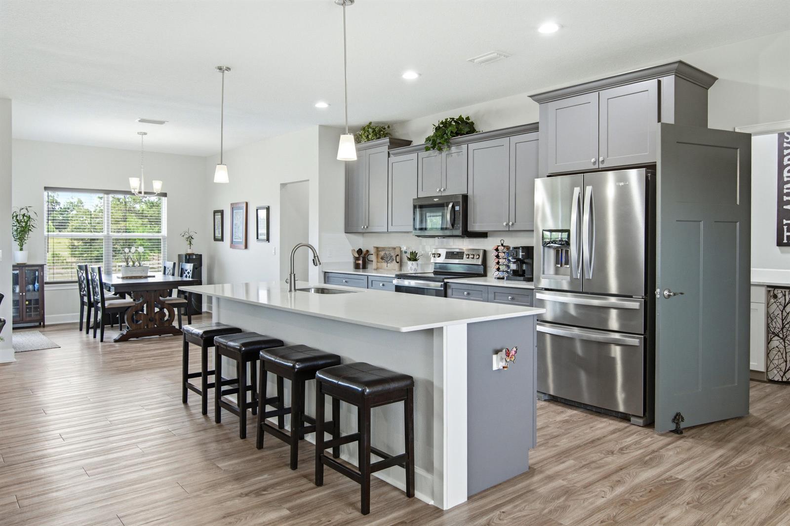 A modern kitchen features gray cabinets, a white quartz island with stools, and stainless appliances — 10172 98th Path # 2, FL 32060, FL