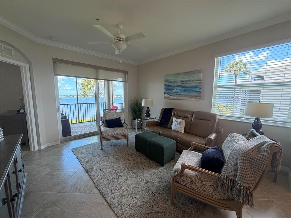 A living room features tile flooring, a beige sofa, two green ottomans, and a balcony view — 920 TIDEWATER SHORES LOOP UNIT 308, BRADENTON, FL