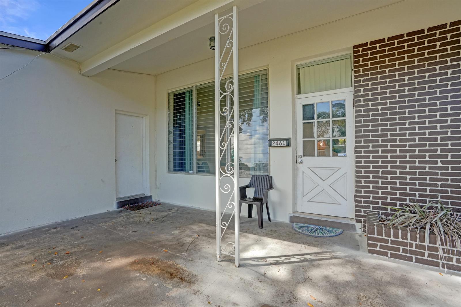 A covered concrete porch features a white decorative metal column, a brick wall, and doors — 2461 NE 20th Avenue, Lighthouse Point FL 33064, LIGHTHOUSE POINT, FL